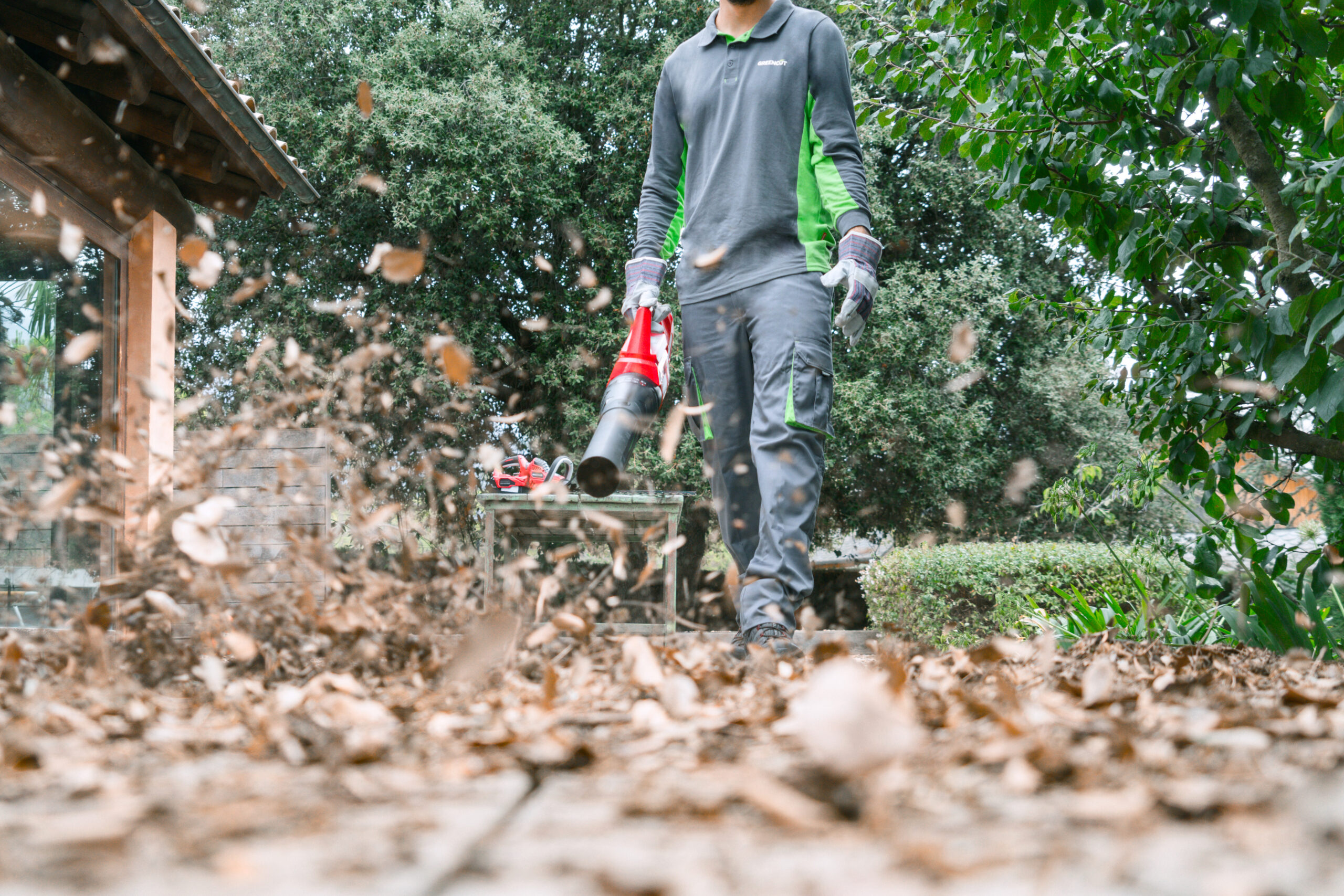 Persona con una máquina sopladora recogiendo las hojas de árbol de su jardín